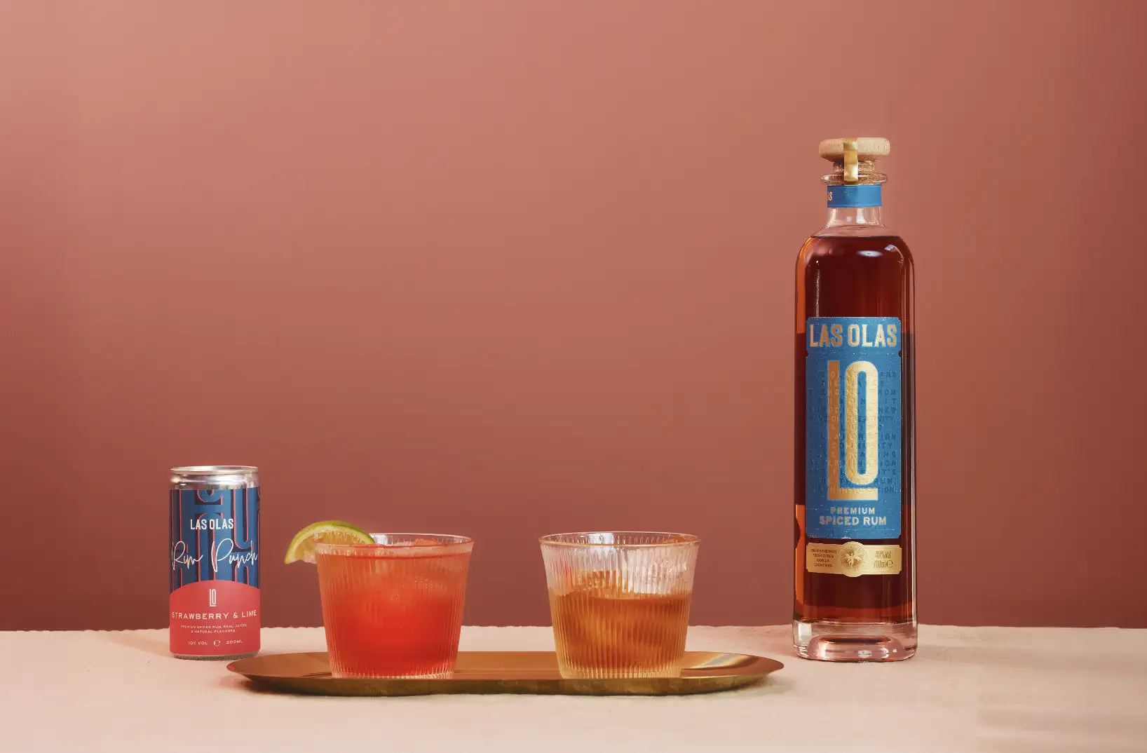 Bottle and can of Las Olas with two cocktails on a tray against a pink background