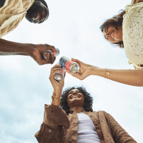 Three people holding cans of las olas rum punch against a clear sky