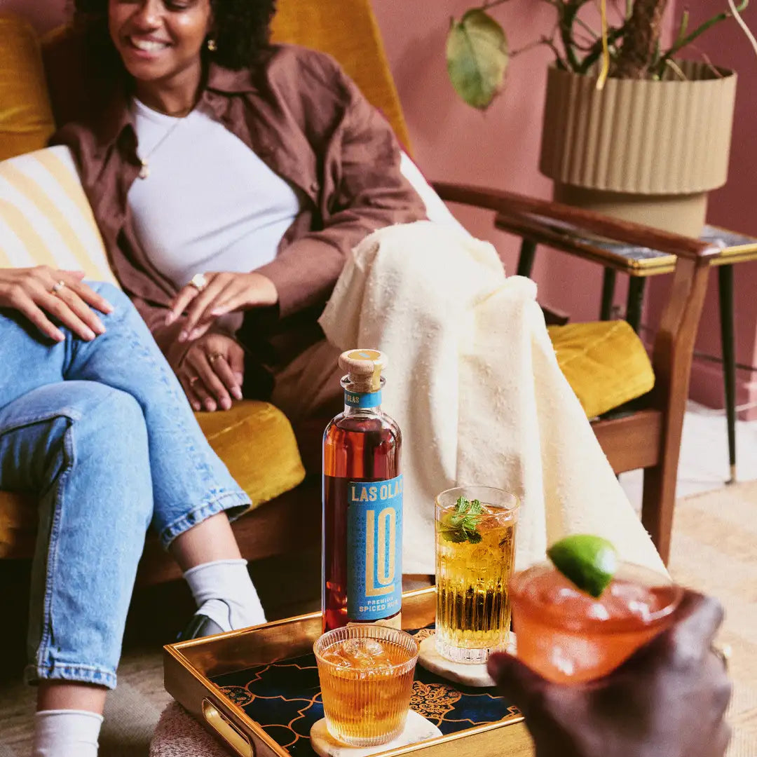 Two people sitting on a couch with drinks and a bottle of las olas premium rum in a cosy living room.