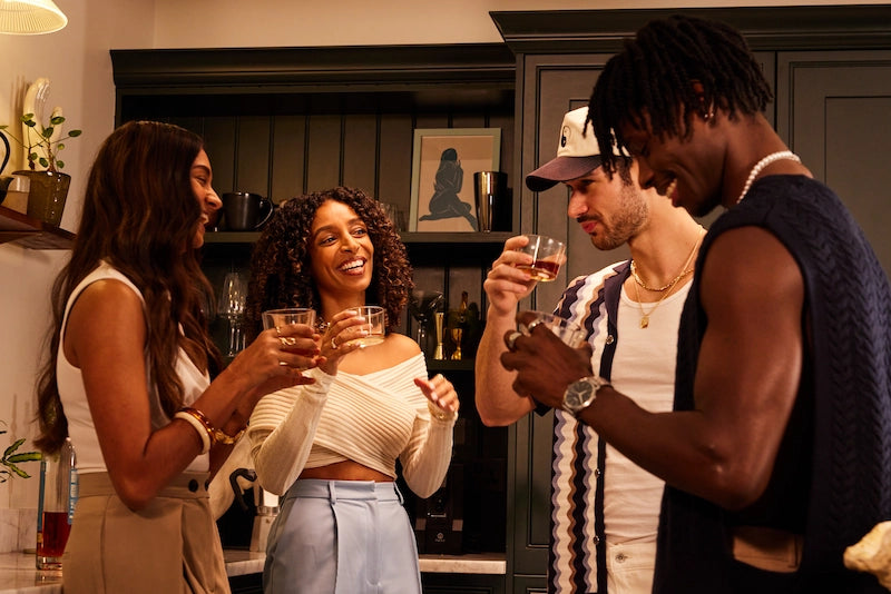 Group of four people socializing and drinking in a kitchen.