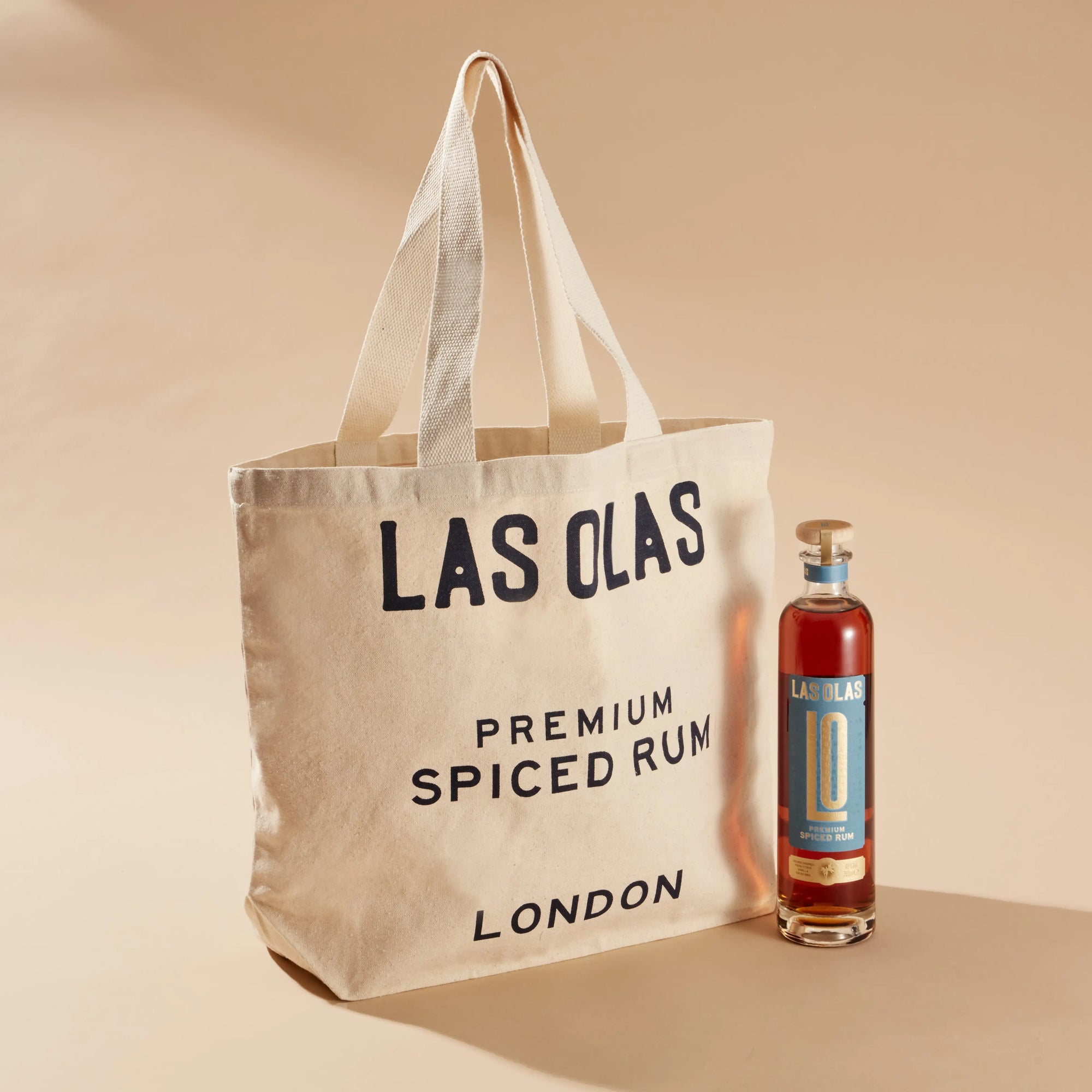 Tote bag with 'Las Olas' branding next to a bottle of spiced rum on a beige background