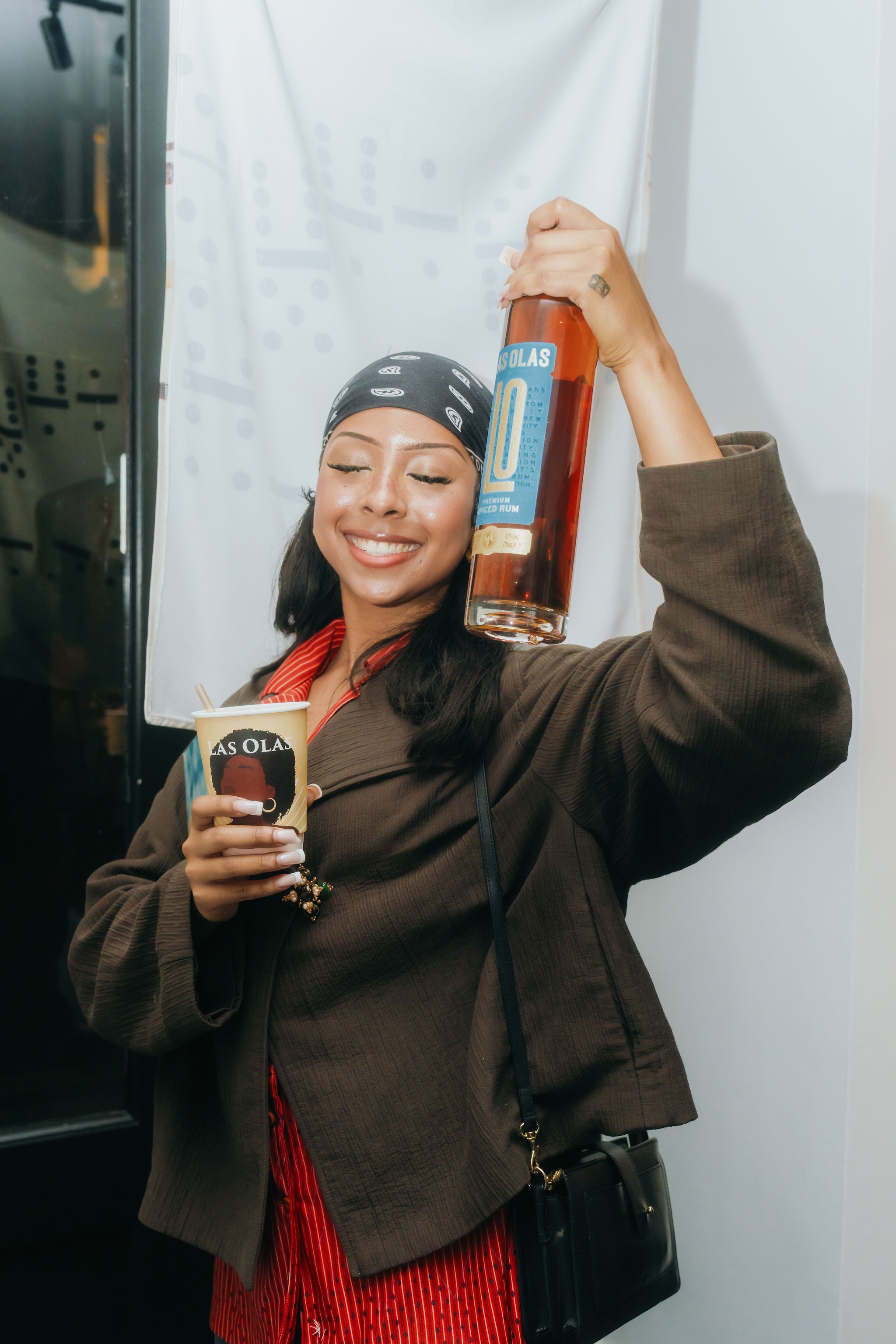 Woman holding a bottle of Las Olas Premium Spiced Rum and a cup, standing against a white wall.