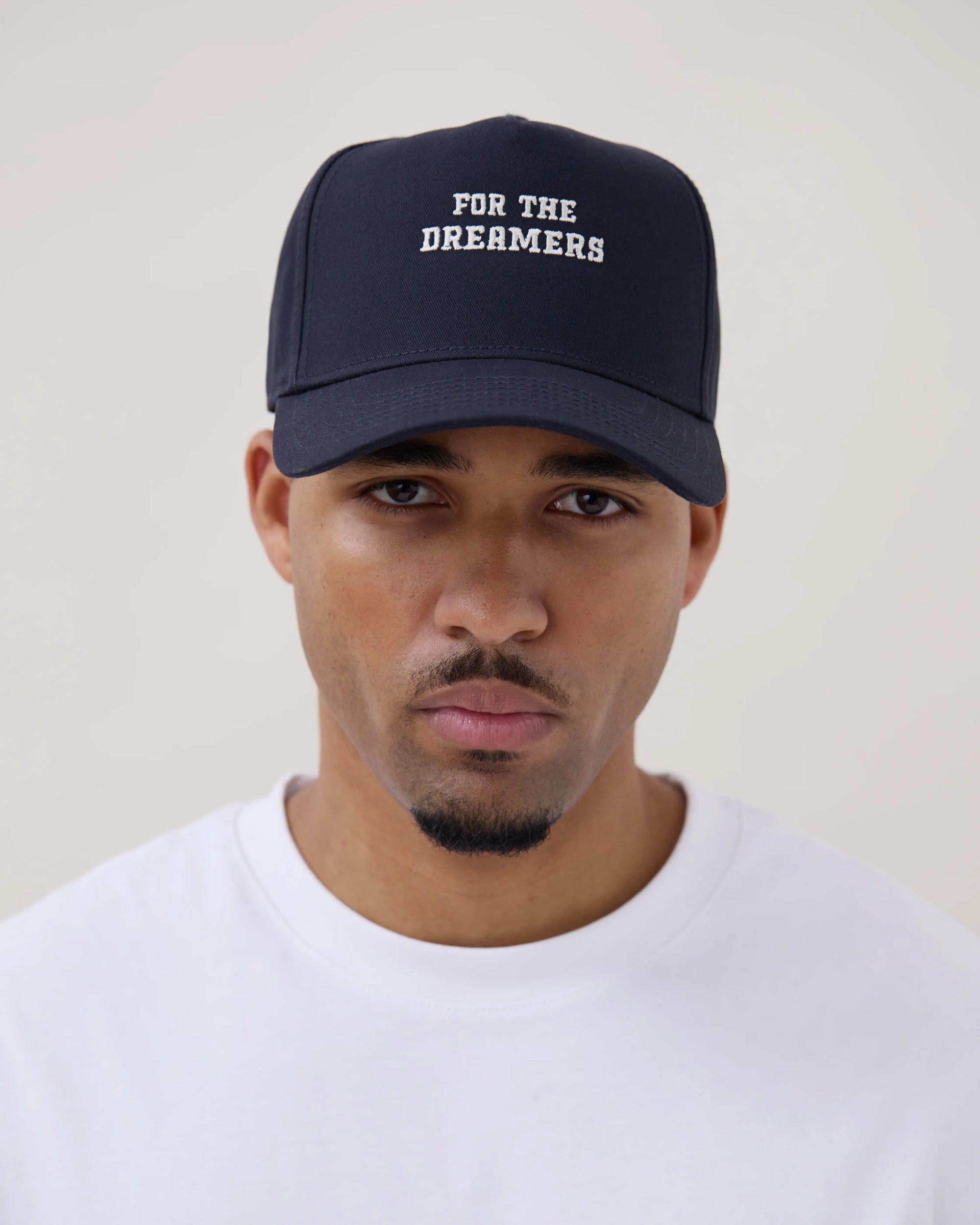 Man wearing a navy blue cap with 'FOR THE DREAMERS' text on a plain background