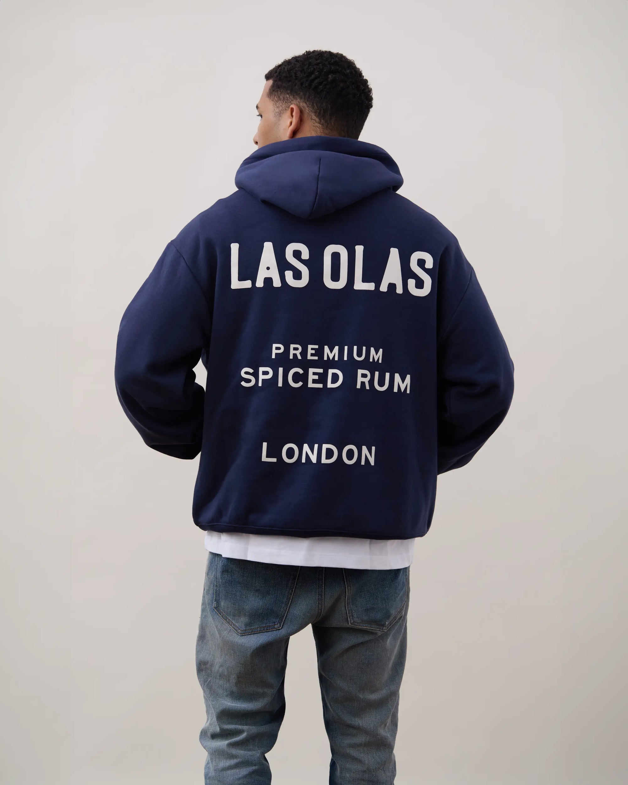 Person wearing a navy hoodie with 'LAS OLAS' branding on the back against a plain background