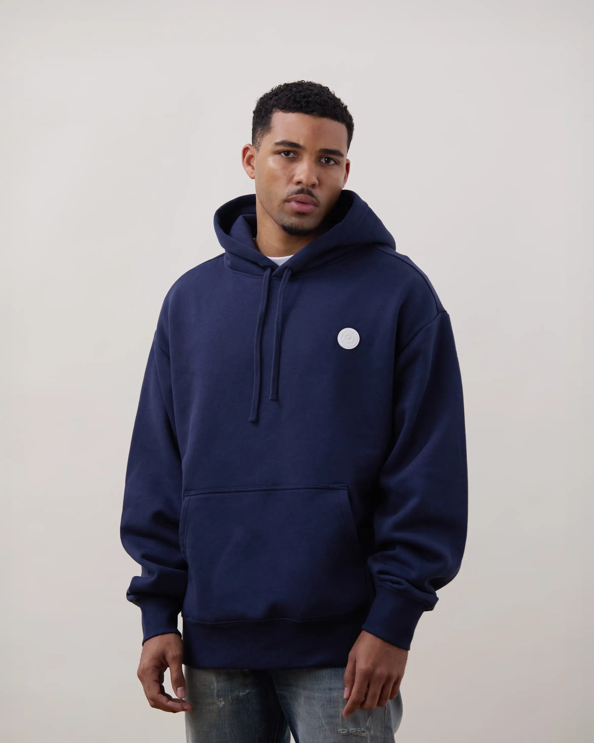 Man wearing a navy blue hoodie with a small white logo on a plain background