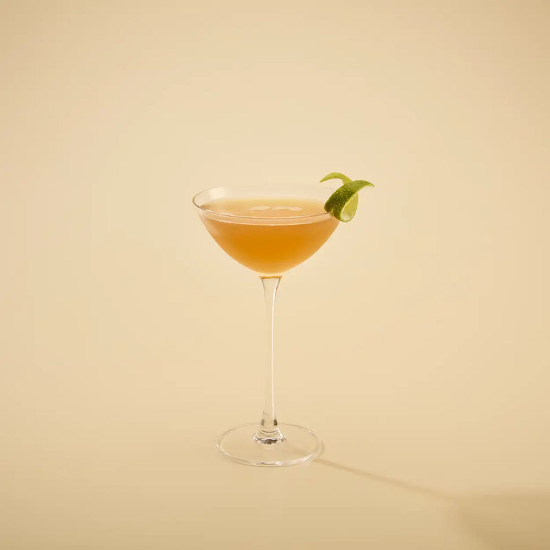 Cocktail in a glass with a lime wedge on a beige background