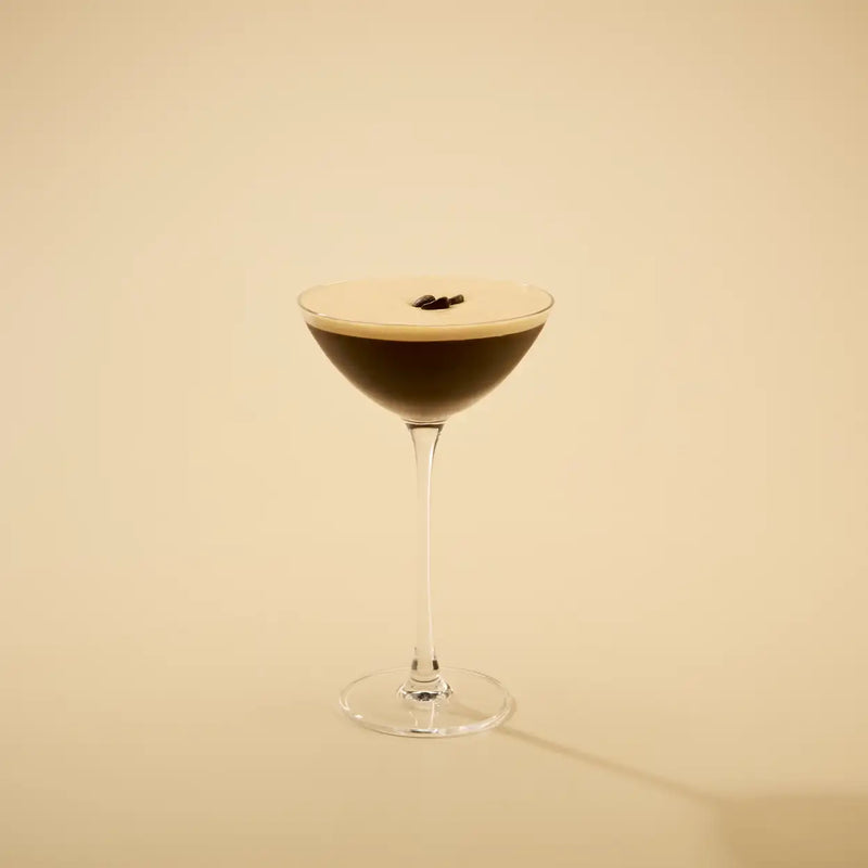 Cocktail in a martini glass with a dark liquid and a light foam layer on a beige background
