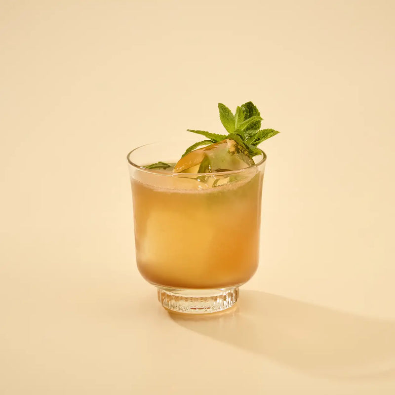 Cocktail with a green garnish in a clear glass on a beige background