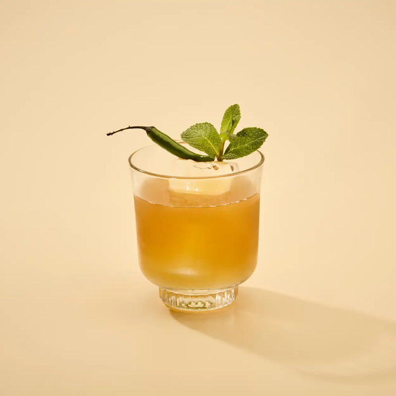 Glass of amber-colored liquid with a green garnish on a beige background