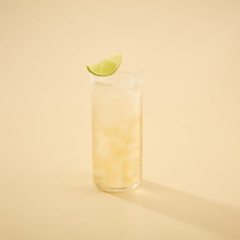 Glass of las olas and tonic with a lime wedge on a beige background