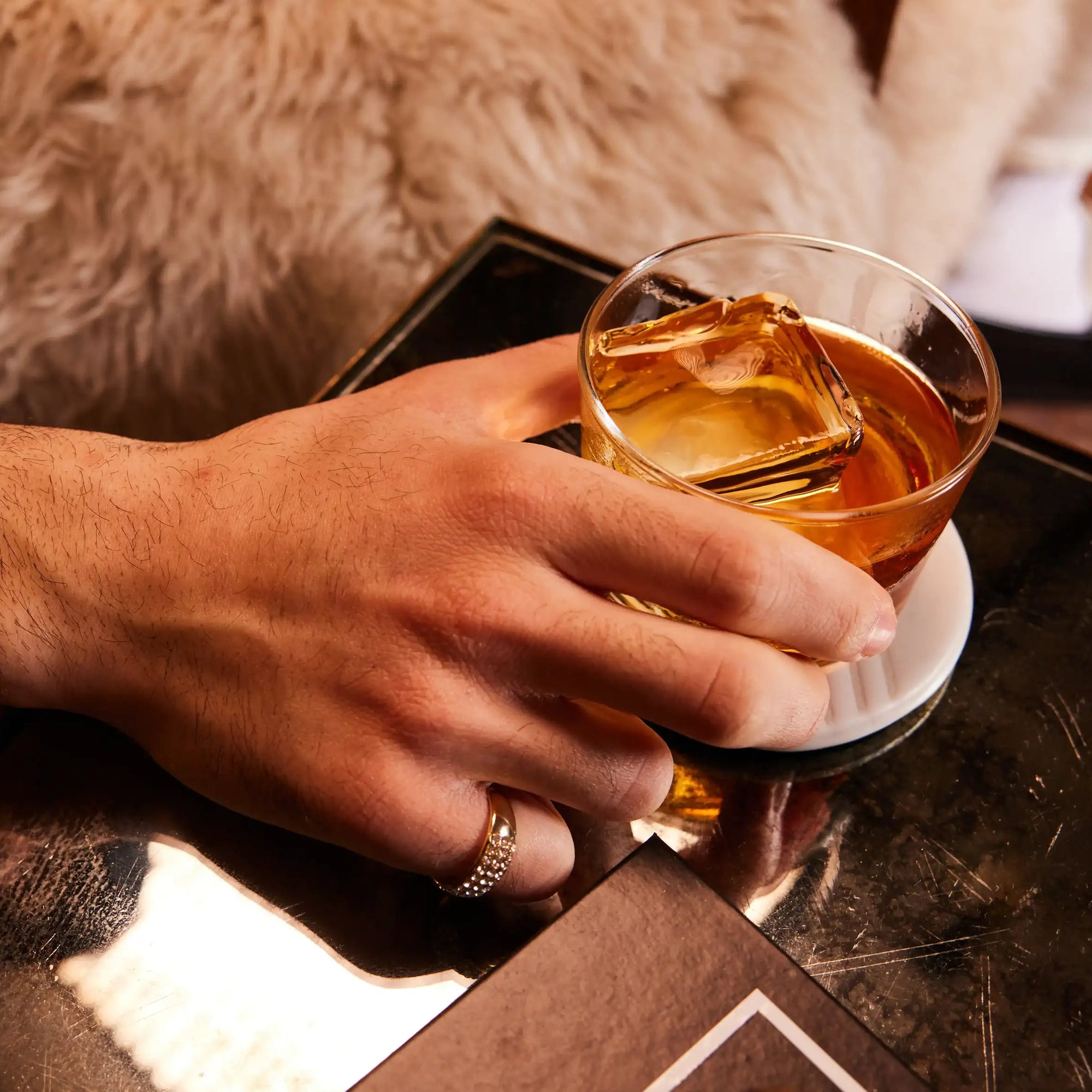 Hand holding a glass of las olas rum with ice on a reflective surface