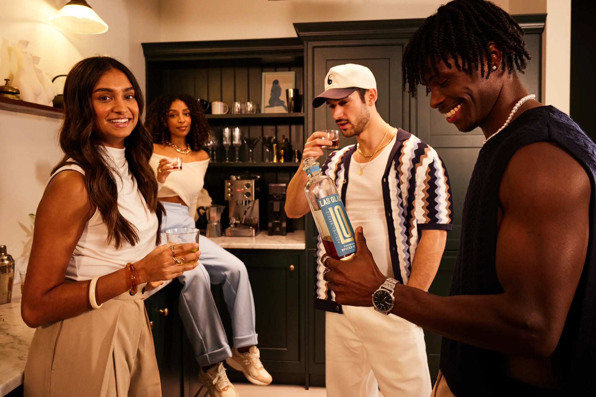 Group of people in a kitchen setting with one person holding a bottle of las olas.