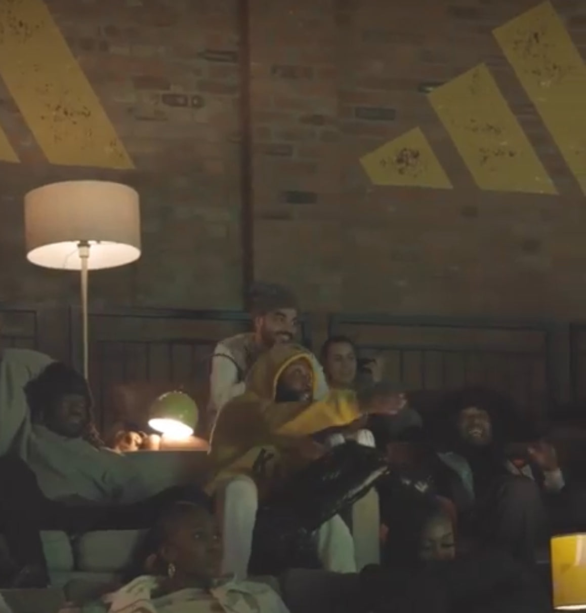 Group of people in a room with a brick wall and yellow adidas posters.