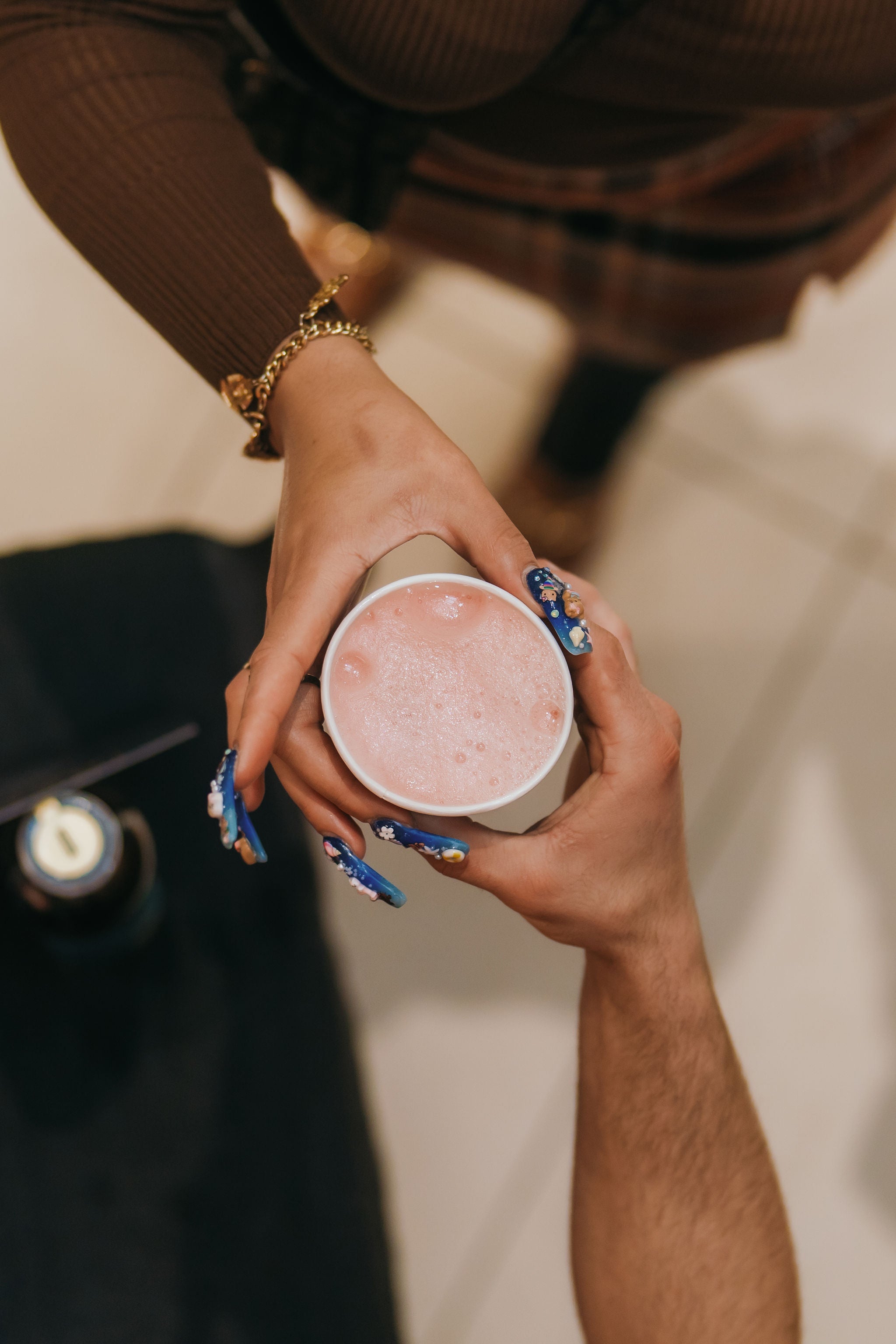 Person holding a pink drink in a paper cup with a blurred background
