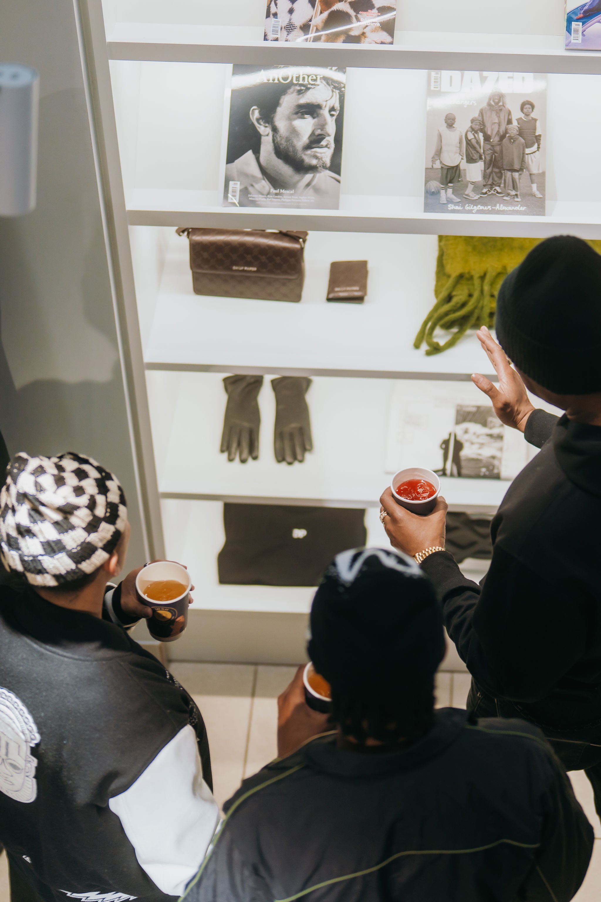 Three people looking at a display case with various items including gloves and a bag.